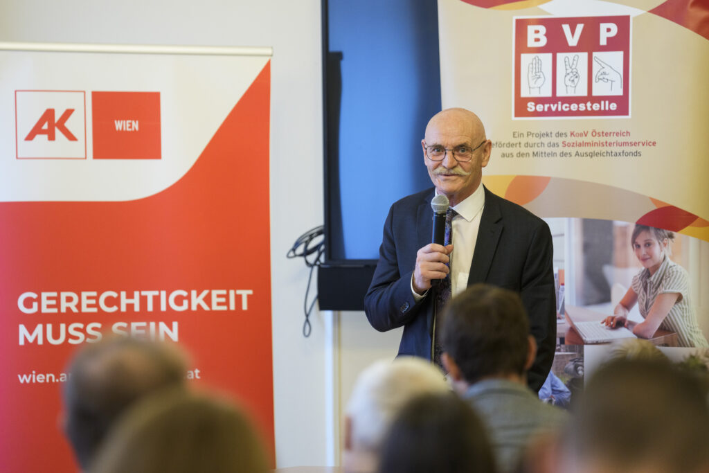 Ein Mann, KOBV-Präsident Franz Groschan, spricht vor einer Gruppe Menschen in ein Mikrofon.