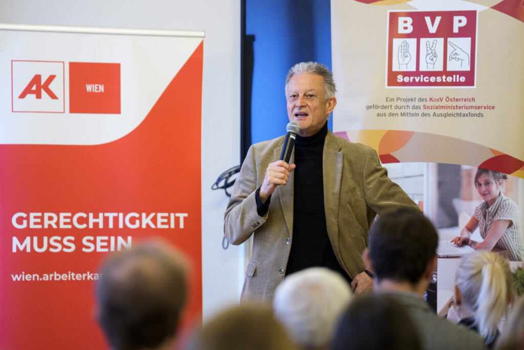 Ein Mann, Hofrat Harald Gruber, Amtsleiter des Sozialministeriumservice, spricht vor einer Gruppe Menschen in ein Mikrofon.