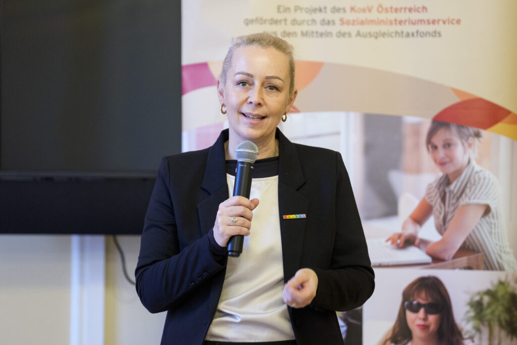 Eine Frau, Mag. Christine Steger, Anwältin für Gleichbehandlungsfragen für Menschen mit Behinderungen, spricht vor einer Gruppe Menschen in ein Mikrofon.