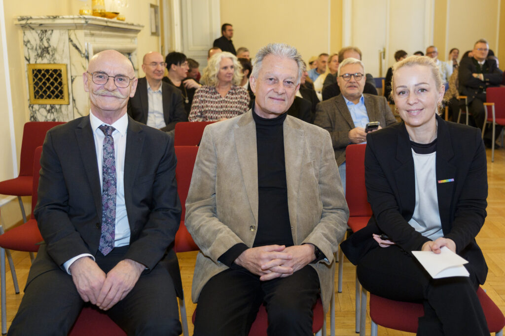 Drei Menschen auf roten Sesseln, Franz Groschan, Hofrat Harald Gruber und Mag. Christine Steger, lächeln in die Kamera.