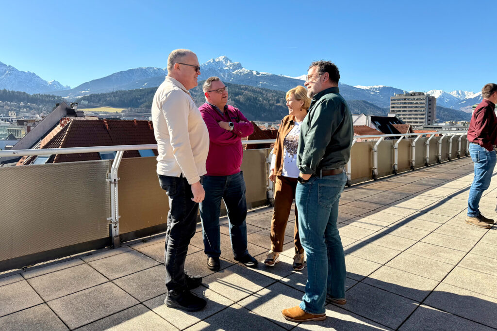 BVP Vernetzungstreffen Tirol Terrasse Vier Menschen unterhalten sich auf der Terrasse eines Gebäudes, im Hintergrund sind die Tiroler Berge zu sehen